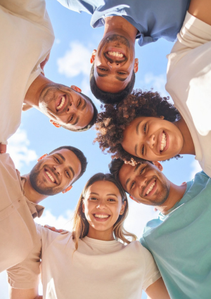 Group of six diverse people looking down at a camera, smiling. blue sky with some clouds in the background.