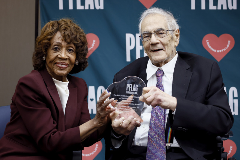 Rep. Maxine Waters is seated next to retired Rep. Barney Frank and together they hold the PFLAG Champion of Justice Award, which is an engraved heart-shaped crystal plaque.