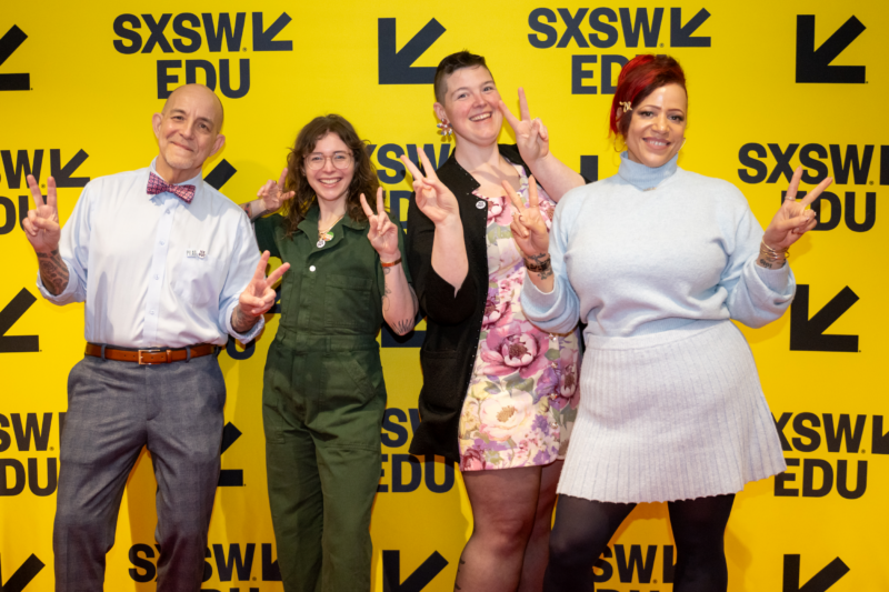 Four smiling people put up their hands with peace signs as they pose in front of a yellow SXSW EDU backdrop. Left to right, Brian Bond has glasses, a bowtie and tattoos; Casey McQuiston has long hair, glasses and tattoos; Sam Helmick has short hair and big flower earrings; and Nicole Hannah-Jones has red hair in a bun with a golden barrette of a serpent holding her fringe.